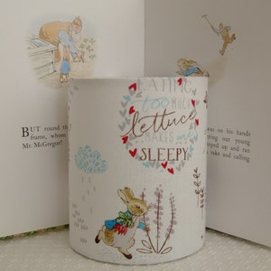May include: White fabric lampshade with a Peter Rabbit design. The lampshade features a quote: "Eating too much lettuce makes me sleepy."