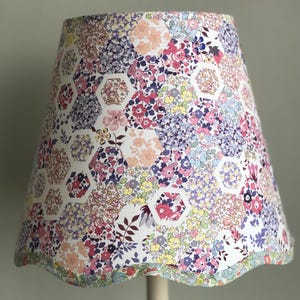 May include: A lampshade featuring a colourful floral design with pink, purple, yellow, and blue hues. The shade has a scalloped edge and a white background with hexagonal shapes.
