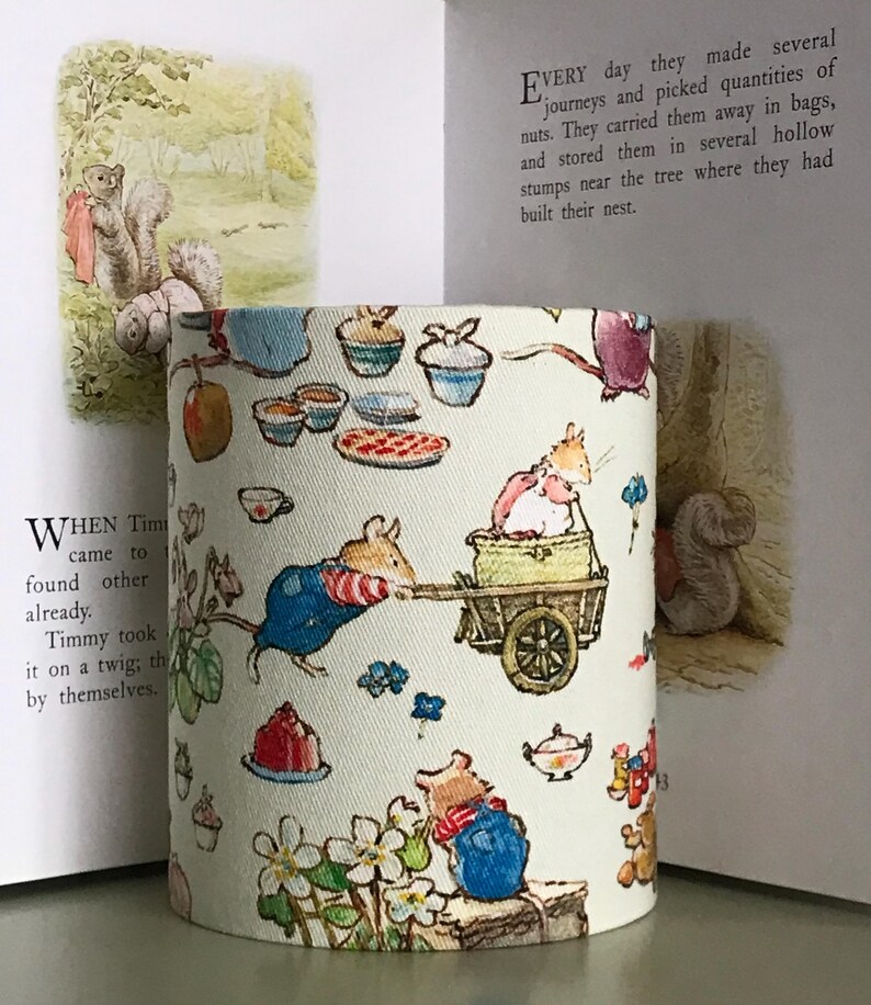 Op de afbeelding: Cilindrische lampenkap met een grillige illustratie van bosdieren, waaronder muizen en eekhoorns, die verschillende activiteiten uitvoeren. Het ontwerp bevat elementen zoals cupcakes, taarten en bloemmotieven, waardoor een sprookjesachtige uitstraling ontstaat.