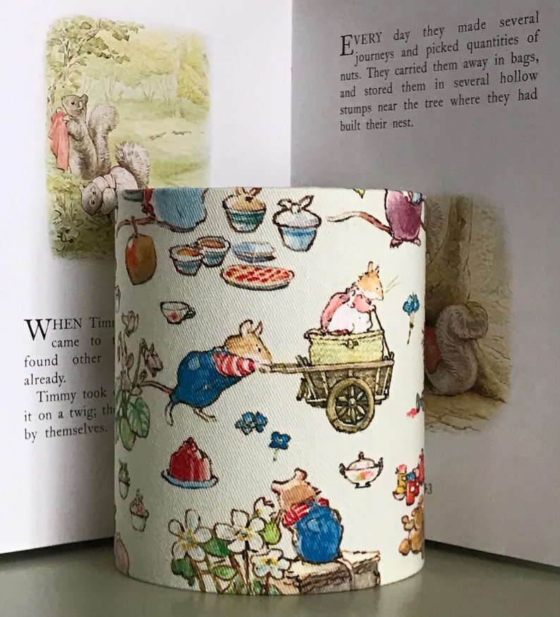 Op de afbeelding: Cilindrische lampenkap met een grillige illustratie van muizen, theekopjes en gebak. Het ontwerp bevat een muis die een kar trekt en andere muizen in overalls. De achtergrond is lichtcr&egrave;me van kleur, met tekst uit een kinderboek zichtbaar.