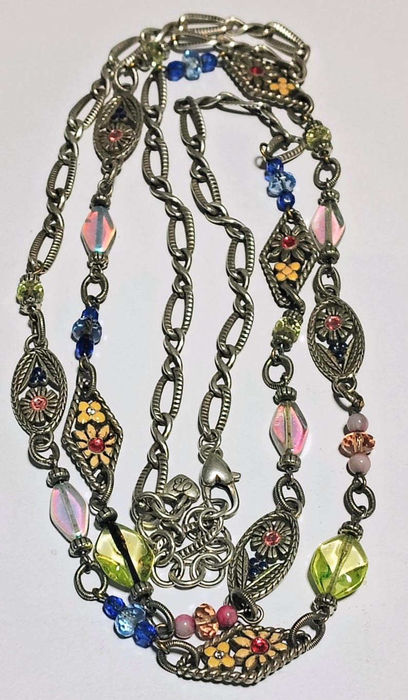 May include: A long silver-tone metal chain necklace featuring oval and diamond-shaped filigree links with floral motifs. The necklace is accented with multi-colored glass beads in shades of blue, pink, yellow, and green, and includes a lobster clasp.