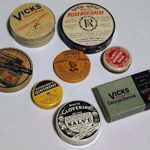May include: A collection of vintage medicinal tins and a box of cough drops. The tins include Vicks VapoRub, Rosebud Salve, Sayman Salve, Peterson's Ointment, and White Cloverine Salve. The cough drops box is green with black text.