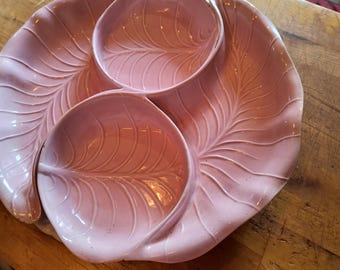 Può includere: Un piatto da portata in ceramica rosa con un motivo a foglie. Il piatto ha tre sezioni, con la sezione esterna a forma di grande foglia e le sezioni interne che assomigliano a foglie più piccole. Il piatto è su una superficie di legno.