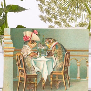 May include: A vintage postcard featuring two anthropomorphic fish dining at a table. The fish are dressed in formal attire, seated at a table with a white tablecloth, wine glasses, and a bottle. The background is a light teal color.