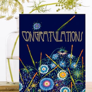May include: A navy blue card with gold glitter and the word "CONGRATULATIONS" in gold lettering. The card features a design of colourful fireworks with blue, green, orange, and pink accents.
