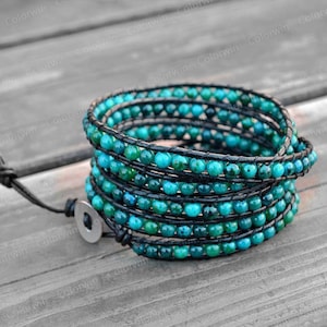 May include: A turquoise and black wrap bracelet with a leather cord and a silver clasp. The bracelet is made of small turquoise beads and is wrapped around the wrist multiple times.