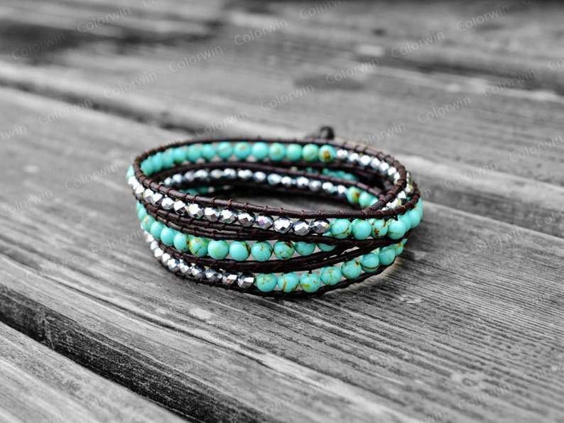 May include: A turquoise and silver beaded wrap bracelet with a brown leather cord. The bracelet is made of small, round beads and is wrapped around the wrist multiple times.