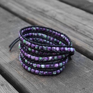 May include: A multi-strand bracelet made of small purple and green beads with black leather wrappings.