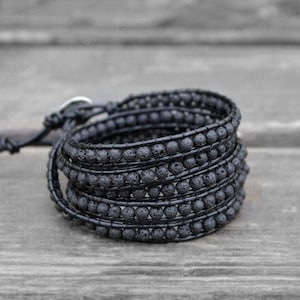 May include: A black lava stone wrap bracelet with a silver clasp. The bracelet is made of multiple strands of small, round beads.