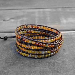 Puede incluir: Un brazalete de múltiples hilos hecho de cuero marrón y pequeñas piedras preciosas redondas multicolores. El brazalete está envuelto alrededor de sí mismo varias veces y tiene un cierre de cuero.