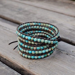 May include: Wrap bracelet featuring turquoise and brown speckled beads. The beads are strung on a dark brown leather cord, wrapped multiple times. The bracelet is secured with a leather tie closure. A stylish accessory.