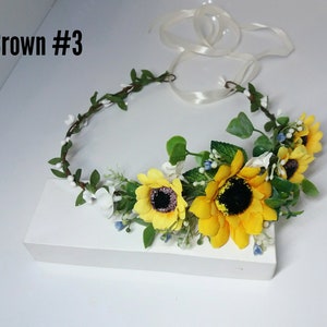 May include: A sunflower and white flower crown with green leaves and white ribbon. The crown is labeled "Crown #3".