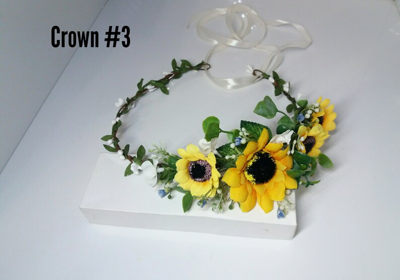 May include: A sunflower and white flower crown with green leaves and white ribbon. The crown is labeled "Crown #3".