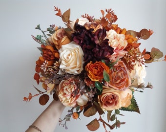 May include: A bouquet of faux flowers in shades of orange, peach, and burgundy. The bouquet includes roses, peonies, and eucalyptus.