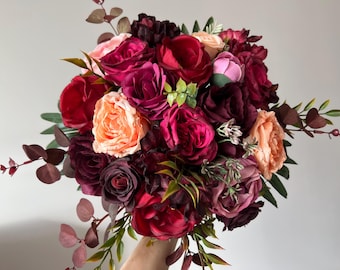 May include: A bouquet of burgundy, red, and peach roses with greenery.