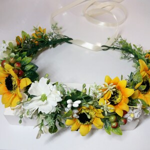 May include: A yellow sunflower flower crown with white flowers and green leaves. The crown is tied with a white ribbon.