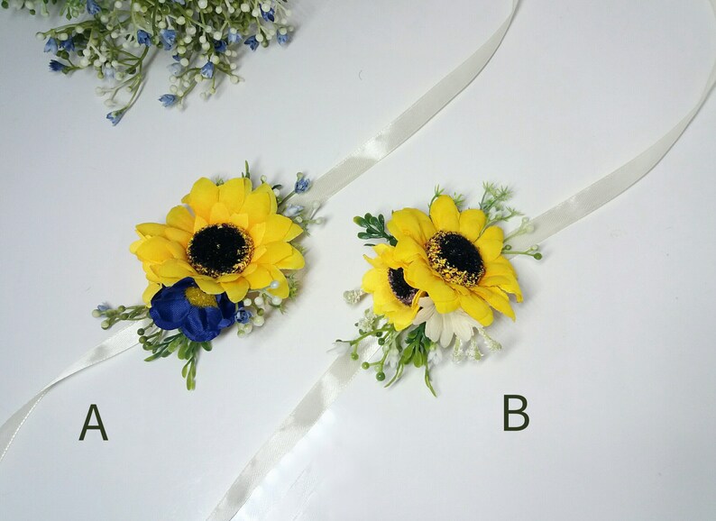 May include: Two sunflower wrist corsages with white ribbon. Corsage A features a blue flower and corsage B features a white flower.