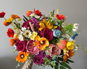 May include: A vibrant bouquet of artificial flowers in a variety of colors, including red, orange, yellow, pink, and purple. The arrangement features roses, poppies, and other blooms, with green foliage.