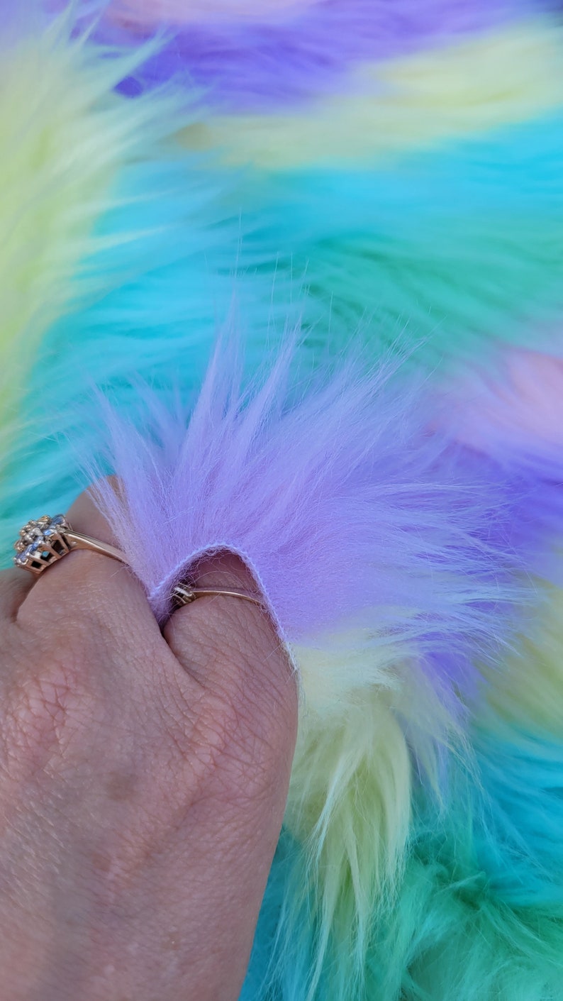 May include: A close-up of a multi-coloured faux fur fabric. The fabric is a gradient of light blue, yellow, and purple.