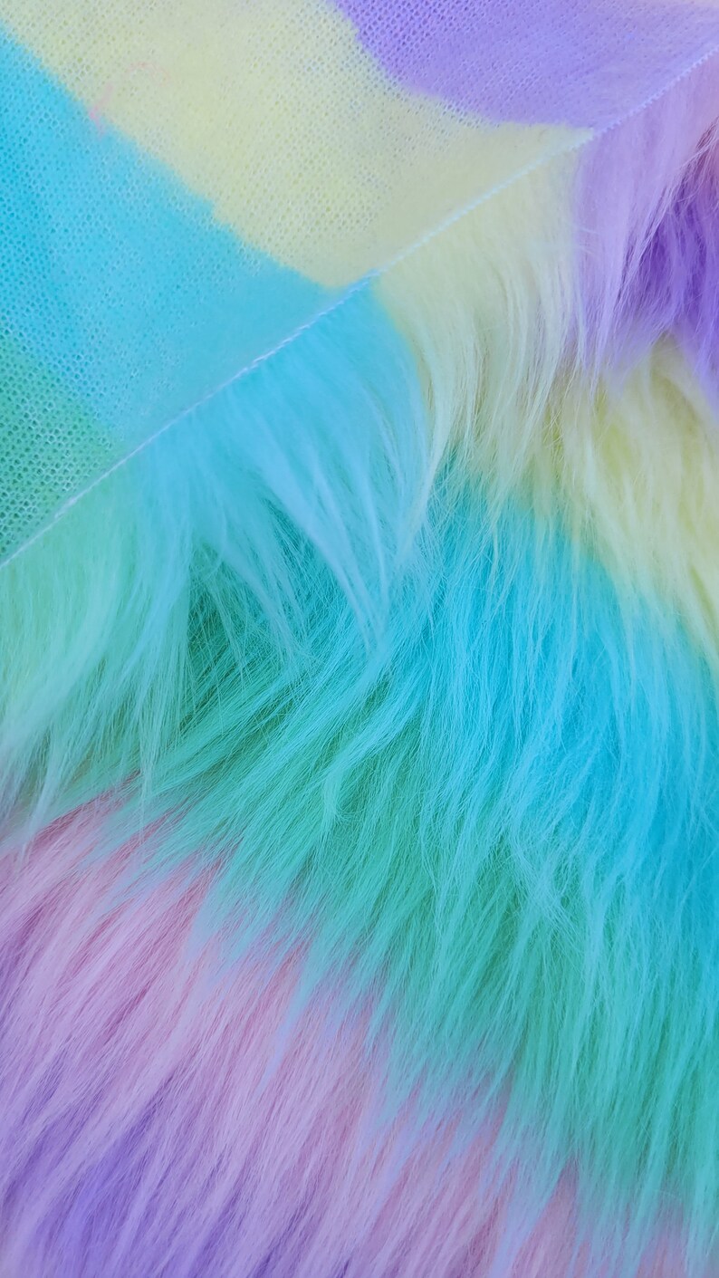 May include: A close-up of a rainbow-coloured faux fur fabric. The fabric is soft and fluffy, with a gradient of colours from purple to blue to green to yellow.