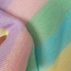 May include: A soft, striped knit fabric in pastel colours, including lavender, pink, green, blue, and yellow. The fabric is folded and shows the texture of the knit.