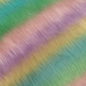 May include: A close-up of a soft, fluffy fabric with a rainbow stripe pattern. The fabric is a mix of pastel colours, including purple, pink, yellow, green, and blue.