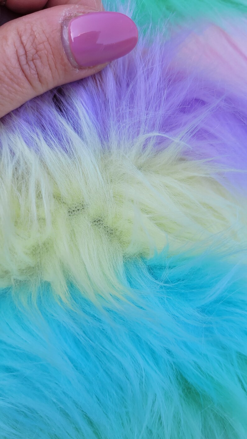 May include: Close-up of a multi-coloured faux fur fabric. The fabric is a gradient of purple, yellow, and blue.