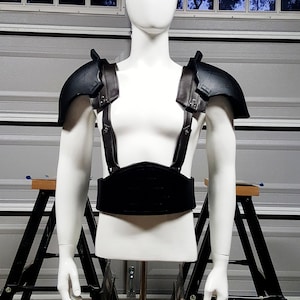 May include: A black leather and metal chest piece with straps. The chest piece is on a white mannequin.