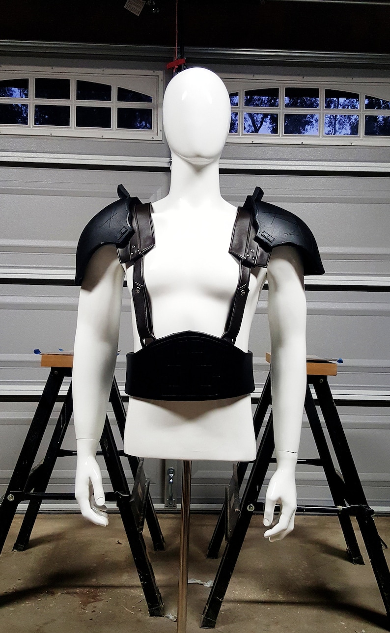 May include: A black leather and metal chest piece with straps. The chest piece is on a white mannequin.