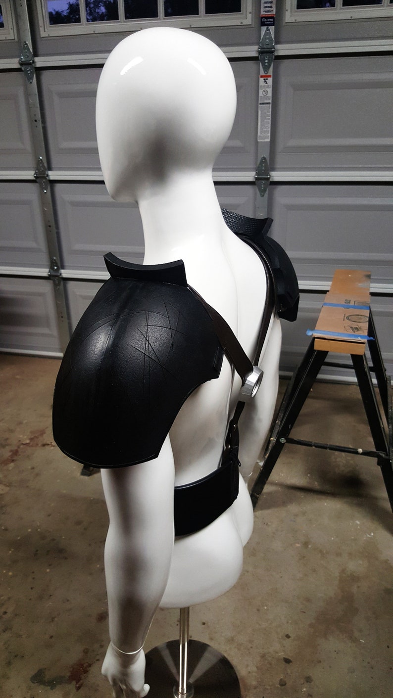 May include: A white mannequin wearing a black leather shoulder armor with straps and a black belt.