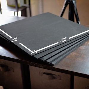 Puede incluir: Una pila de ocho cuadrados de espuma negra, cada uno mide aproximadamente 50 cm por 50 cm. Los cuadrados de espuma est&aacute;n apilados sobre una mesa de madera.