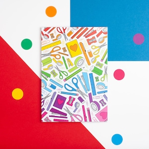 Puede incluir: Un fondo blanco con un patrón colorido de útiles escolares, incluyendo tijeras, lápices, reglas y borradores. El patrón se repite en una hoja de papel blanca con un corazón rojo en el centro.