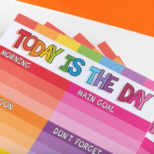 Puede incluir: Un planificador diario de colores arco&iacute;ris con el texto "TODAY IS THE DAY" en letras negritas y coloridas. El planificador tiene secciones para "Morning", "Afternoon", "Main Goal" y "Don't Forget".