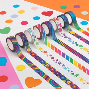 Puede incluir: Una variedad de rollos de cinta adhesiva decorativa washi con varios patrones coloridos, incluyendo arco&iacute;ris, flores, estrellas y rayas. La cinta est&aacute; desenrollada, revelando los dise&ntilde;os. El fondo presenta recortes de papel coloridos.