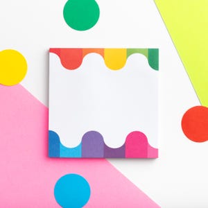 May include: A square white notepad with a rainbow-colored wavy border. The design features a spectrum of colors, including red, orange, yellow, green, blue, and purple. The notepad is surrounded by colorful geometric shapes on a white and pink background.