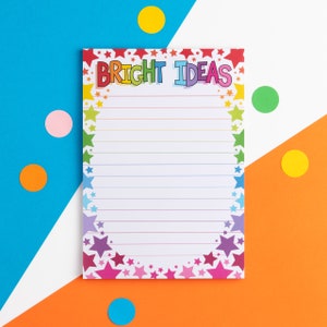 以下が含まれることがあります： 虹色の星形の縁取りと「BRIGHT IDEAS」というカラフルな文字が書かれた白いメモ帳。メモ帳は青とオレンジの背景にカラフルな円が置かれている。