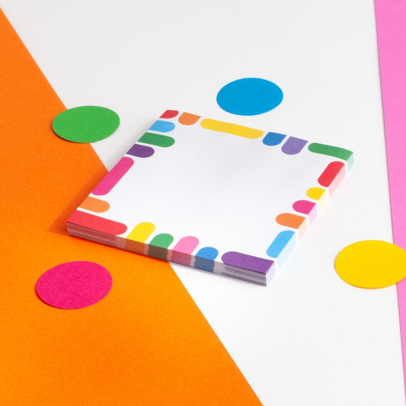 May include: A stack of colorful notepad paper with a rainbow border. The paper is on a white surface with orange, pink, green, blue, and yellow circles.