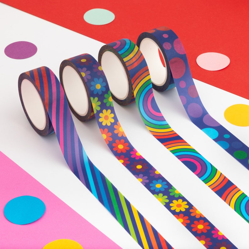 Puede incluir: Cuatro rollos de cinta adhesiva decorativa con patrones coloridos. Los dise&ntilde;os incluyen rayas diagonales, flores, c&iacute;rculos de arco&iacute;ris y lunares. La cinta est&aacute; sobre un fondo blanco y rojo con confeti colorido.