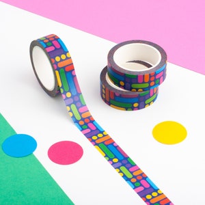 Puede incluir: Dos rollos de cinta washi estampada de colores con un diseño geométrico. La cinta está sobre una superficie blanca con un fondo rosa y verde. Hay tres círculos de colores en la superficie.