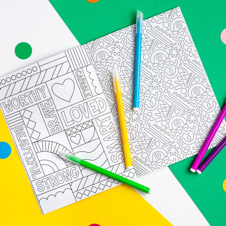 Puede incluir: Un libro para colorear con un dise&ntilde;o en blanco y negro que incluye palabras como "digno", "valiente", "amado", "capaz" y "inteligente". El libro est&aacute; abierto sobre una superficie amarilla y hay cinco marcadores de colores junto a &eacute;l.
