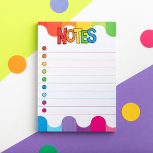 Puede incluir: Un bloc de notas rectangular con la palabra «NOTES» en colores arcoíris en la parte superior. El bloc de notas tiene un fondo blanco con líneas horizontales y puntos de colores para listas de verificación. Los bordes del bloc de notas tienen un diseño ondulado de arcoíris.