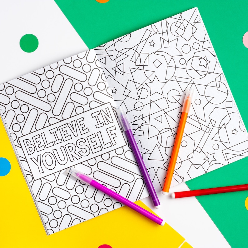 Puede incluir: Un libro para colorear con un patr&oacute;n geom&eacute;trico en blanco y negro en un lado y la frase "Cree en ti mismo" en el otro lado. El libro est&aacute; abierto y hay cuatro marcadores de colores encima.