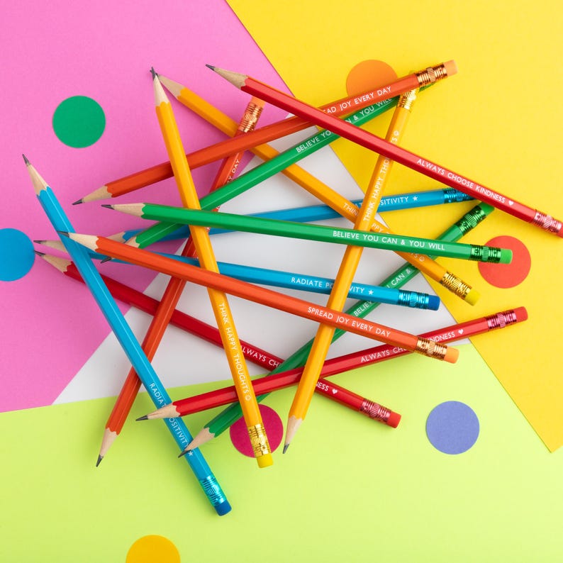 Pu&ograve; includere: Una collezione di matite colorate con frasi motivazionali come "Believe You Can & You Will" e "Always Choose Kindness" stampate sopra. Le matite, in rosso, blu, verde e giallo, sono disposte su uno sfondo vivace.