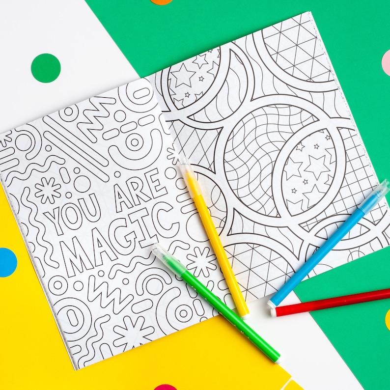 Puede incluir: Dos p&aacute;ginas para colorear con ilustraciones en blanco y negro. Una p&aacute;gina presenta un patr&oacute;n geom&eacute;trico con el texto "You Are Magic". La otra p&aacute;gina presenta un patr&oacute;n de c&iacute;rculos y estrellas. Cuatro marcadores de colores est&aacute;n encima de las p&aacute;ginas.