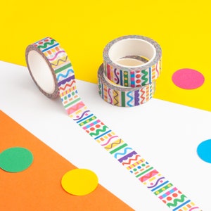 Puede incluir: Rollos de cinta adhesiva washi decorativa con patrones geométricos coloridos en rosa, verde, azul y amarillo. Un rollo está desenrollado, revelando el patrón. El fondo es una mezcla de blanco, naranja y amarillo.