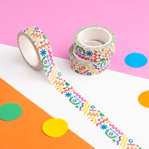 May include: A roll of colorful washi tape with a geometric pattern. The tape is unrolled and shows the design, which includes circles, lines, and stars. The tape is on a pink, white, and orange background with colorful circles.