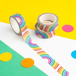 May include: Three rolls of rainbow patterned washi tape. The tape is on a yellow, white, and green background with colorful circles.
