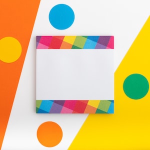 May include: A white card with a colourful rainbow patterned border sits on a white surface with yellow, orange, blue and green circles around it.