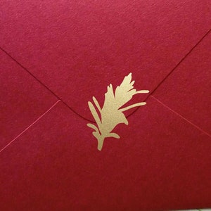 May include: A red envelope with a gold-colored floral design on the front. The envelope is sealed and has a textured surface. The background is a floral pattern on a wooden surface.