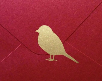 Pode incluir: Um envelope vermelho com uma silhueta de pássaro dourada na frente.